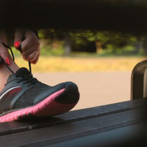 Woman in Black and Pink Sneaker Tying Lace of Her Shoe